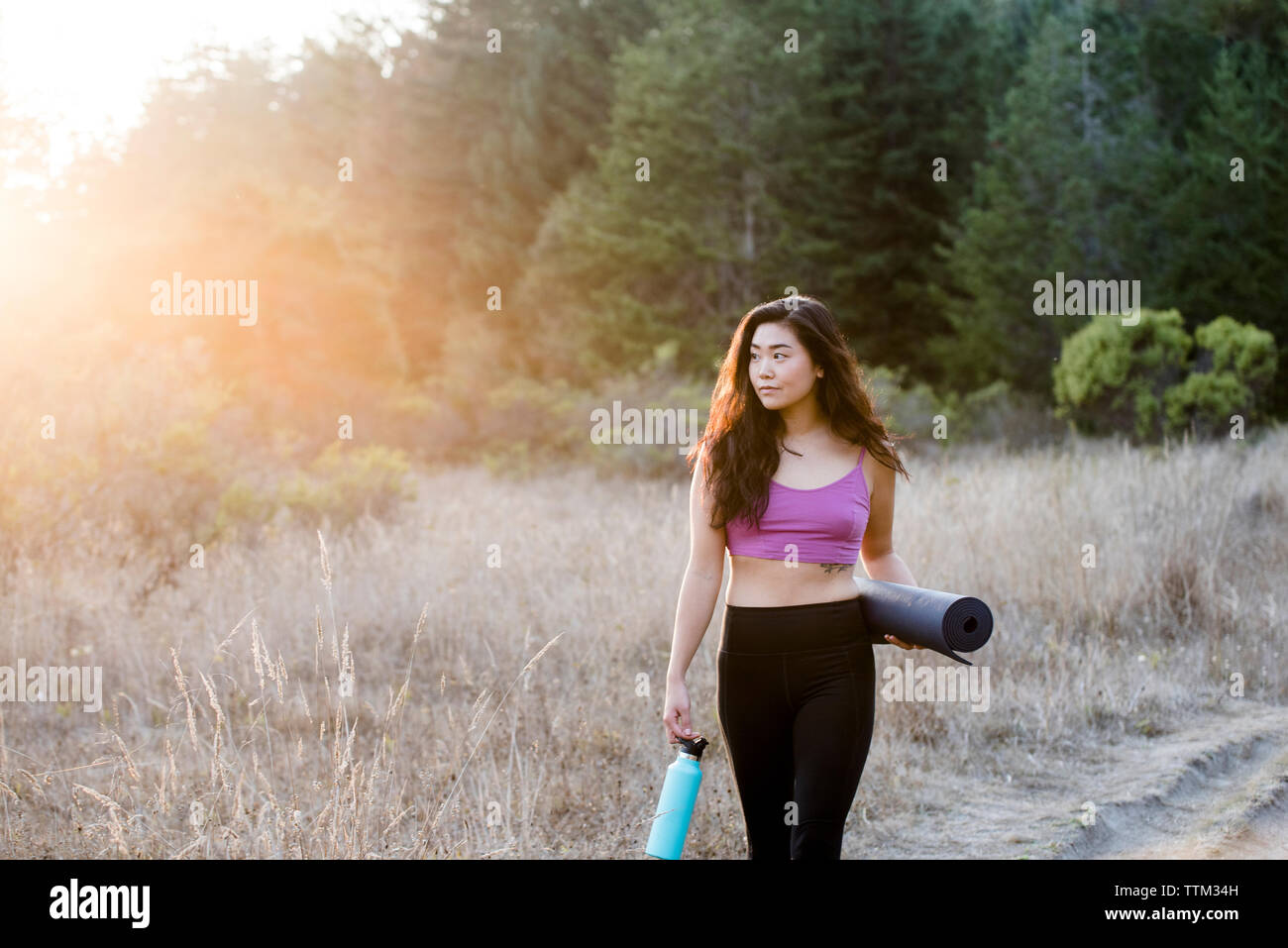 Donna che mantiene esercizio mat e una bottiglia d'acqua mentre si cammina nel campo Foto Stock
