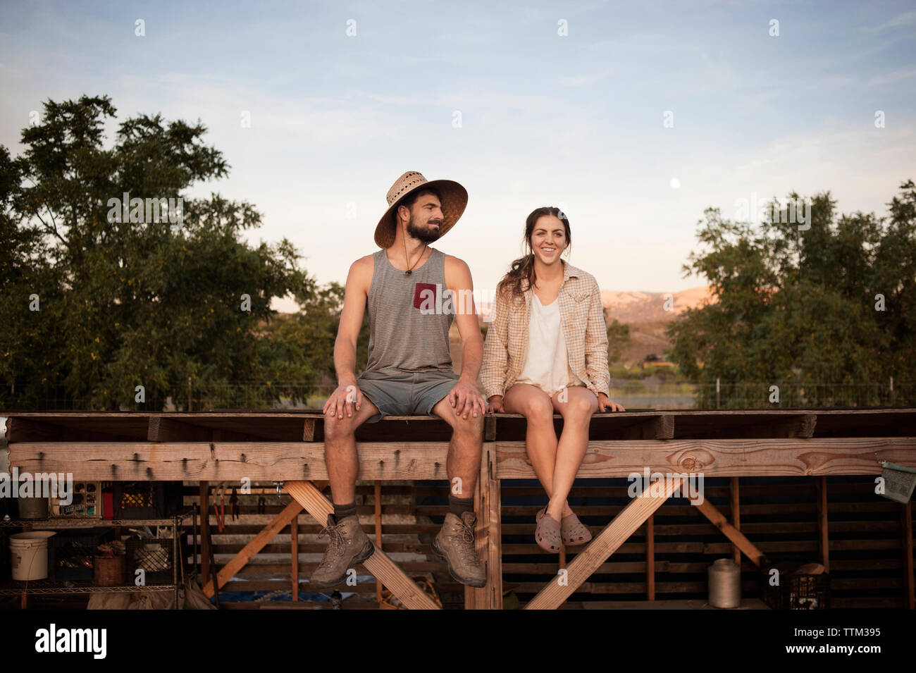 Felice agricoltore femmina seduta con uomo sulla struttura in legno presso l'azienda Foto Stock