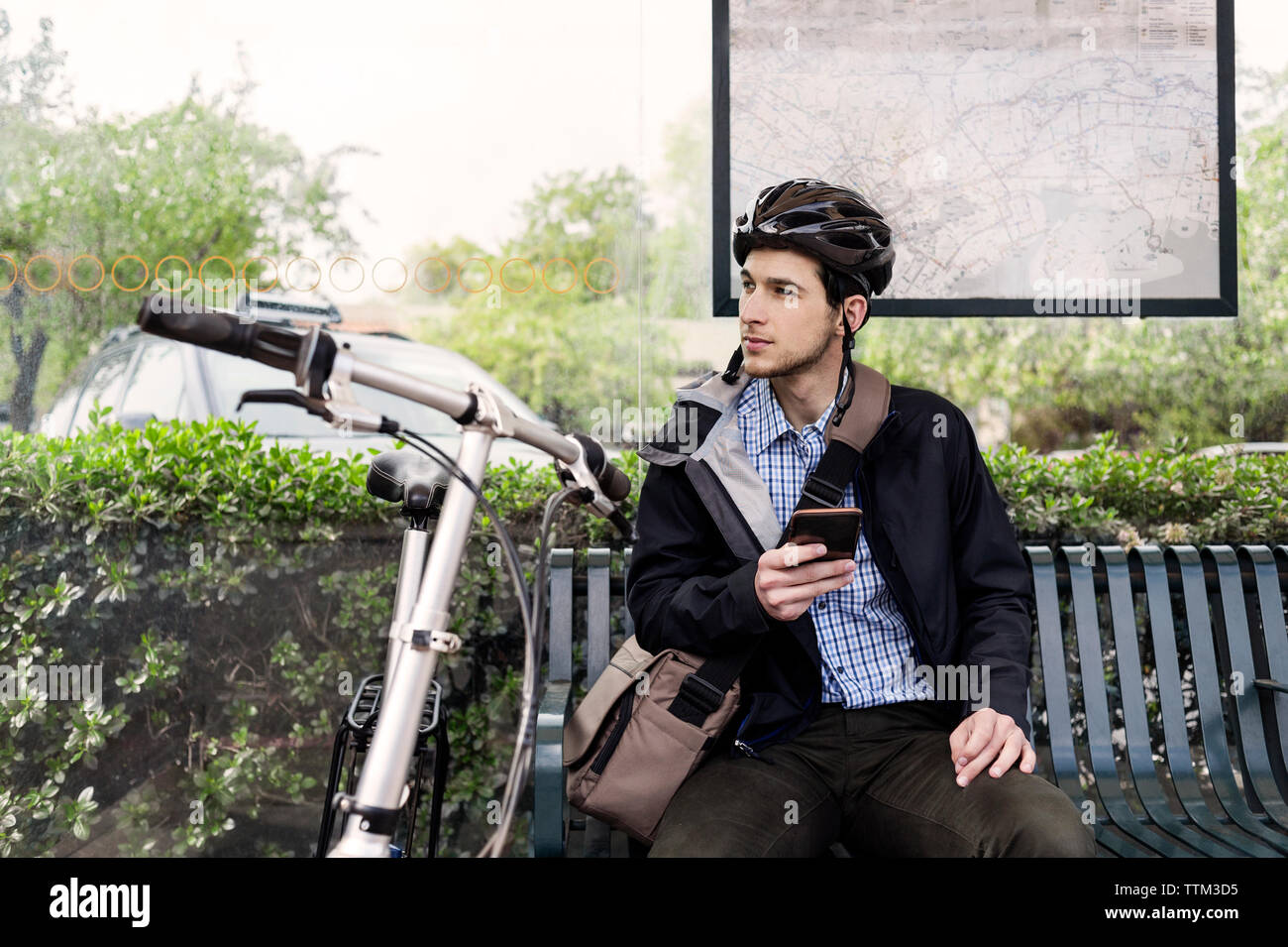 Giovane maschio holding di " commuters " smart phone mentre è seduto alla fermata del bus Foto Stock