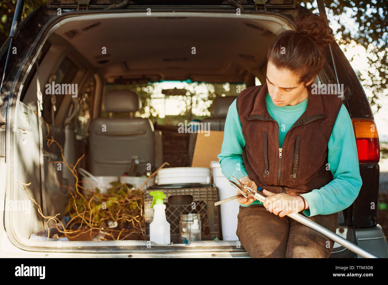 Donna esaminando utensile da giardinaggio mentre sedendo nel baule auto Foto Stock