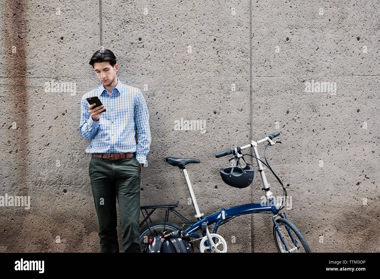 uomo d'affari che utilizza lo smartphone mentre si trova in bicicletta contro il muro Foto Stock