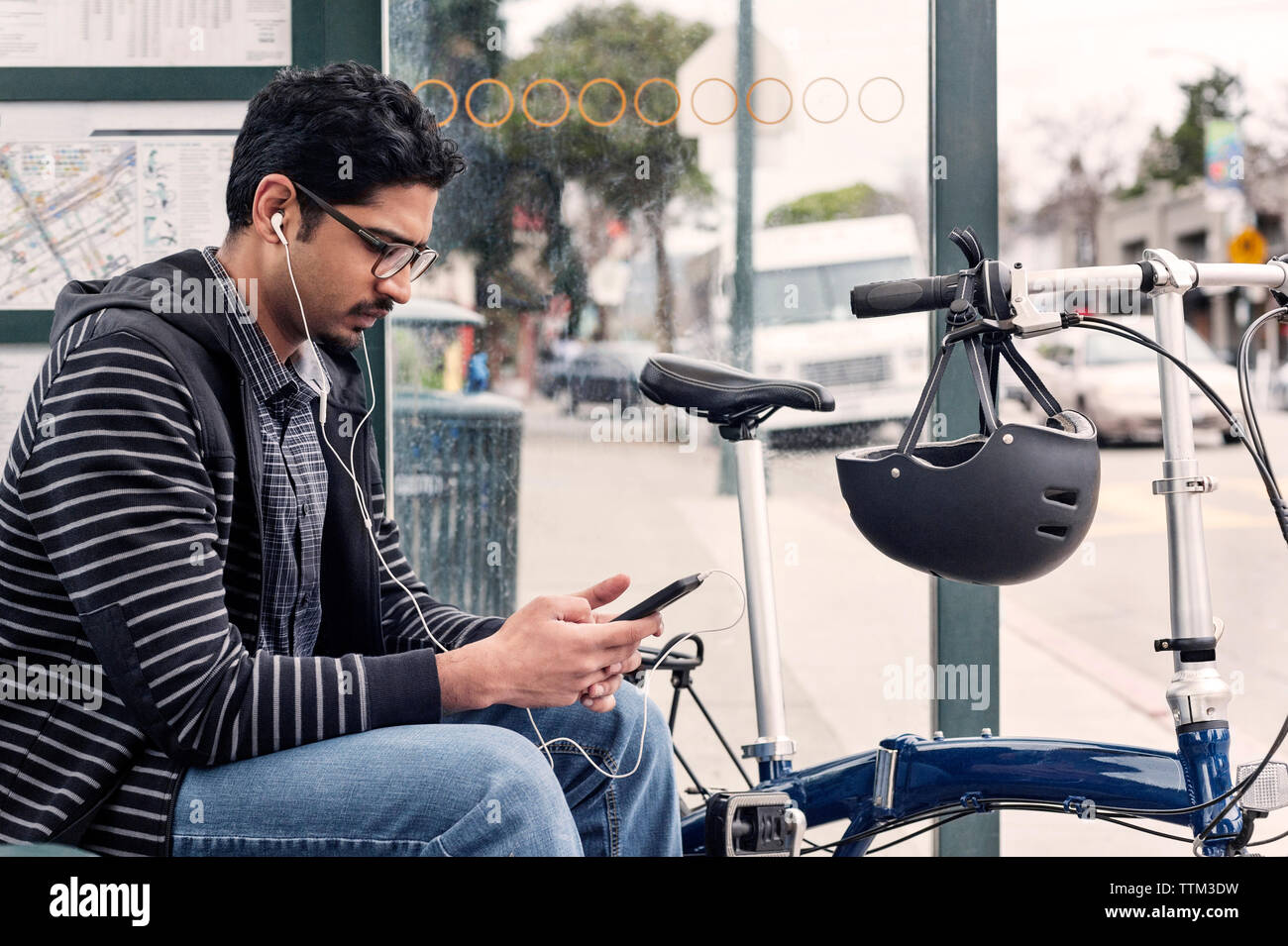 Di " commuters " maschio utilizzando smart phone mentre è seduto con la bicicletta alla fermata del bus Foto Stock