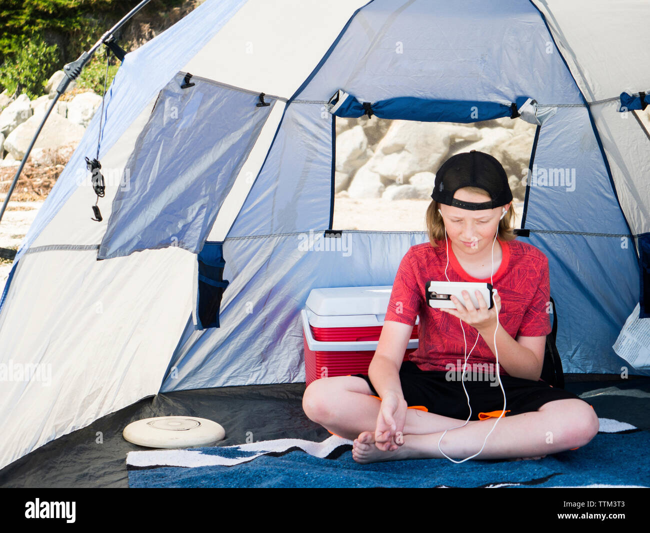 Boy utilizzando smart phone mentre è seduto in tenda Foto Stock