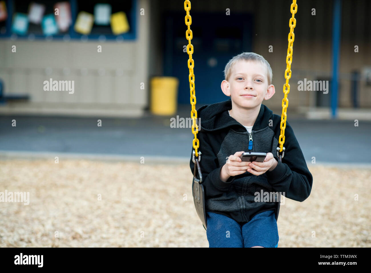 Ritratto di boy utilizzando il telefono cellulare durante l'oscillazione in posizione di parcheggio Foto Stock