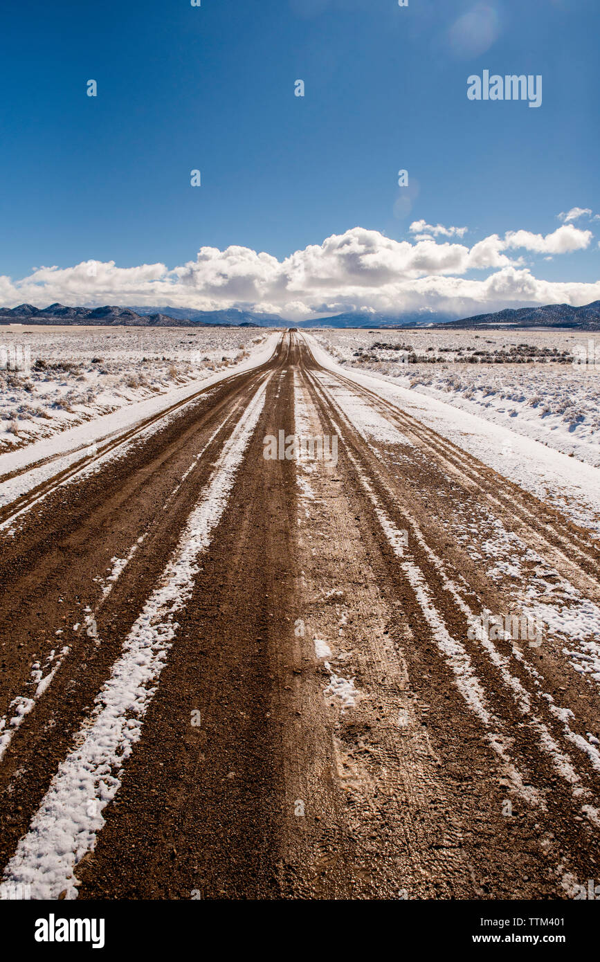 Strada sterrata in mezzo al deserto nevoso contro sky durante il periodo invernale Foto Stock
