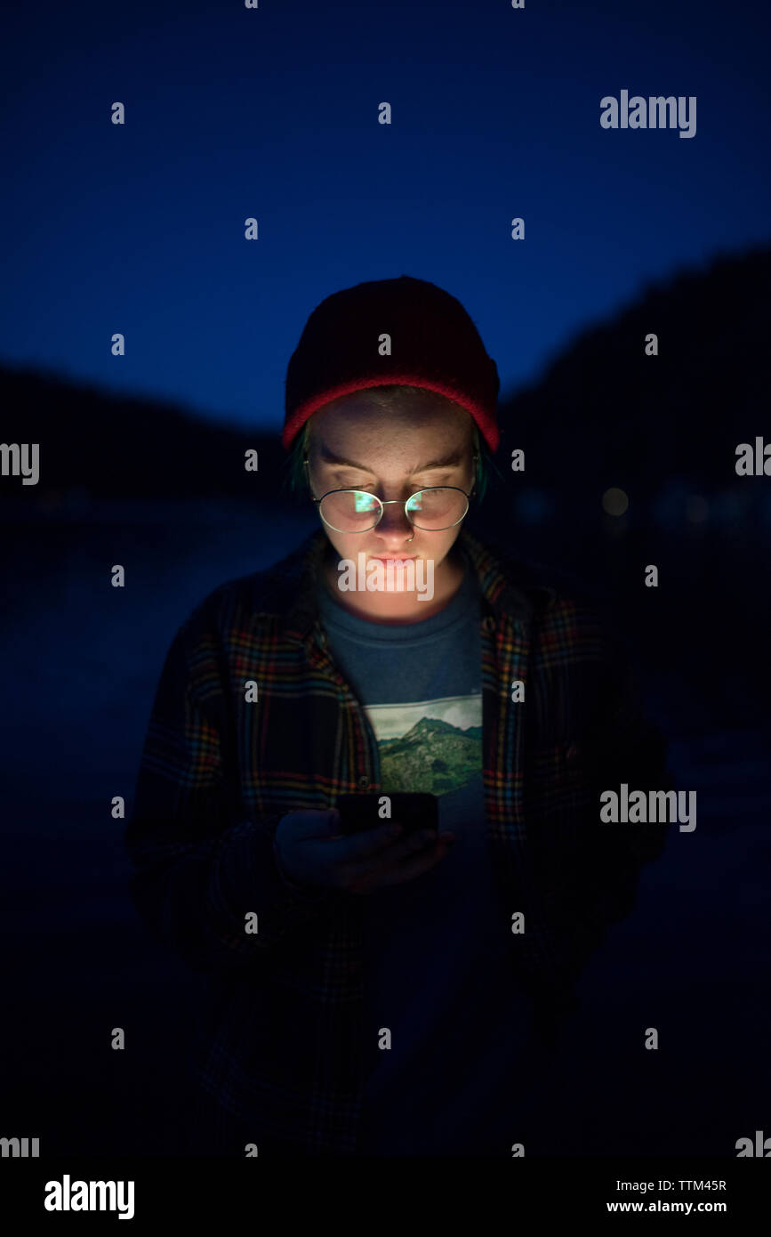 Ragazza adolescente usando il cellulare mentre in piedi contro il cielo nel Parco Nazionale di Olympic di notte Foto Stock