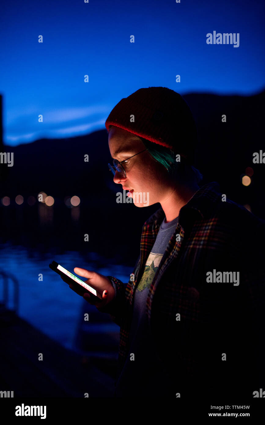 Ragazza adolescente usando il cellulare mentre in piedi contro il cielo blu nel Parco Nazionale di Olympic di notte Foto Stock