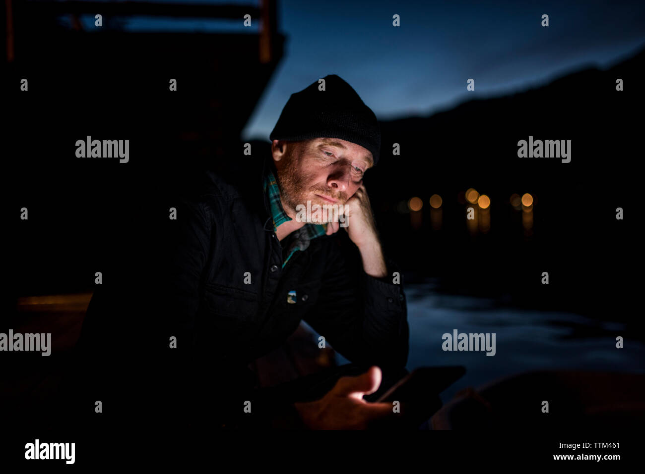 Uomo che utilizza smart phone mentre è seduto sul lungolago contro sky nel Parco Nazionale di Olympic di notte Foto Stock