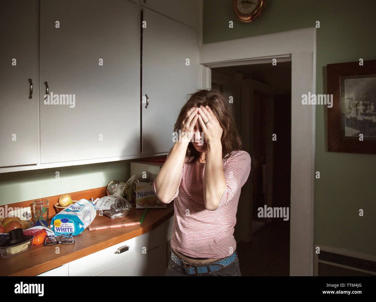 La donna che soffre di mal di testa in piedi in cucina Foto Stock