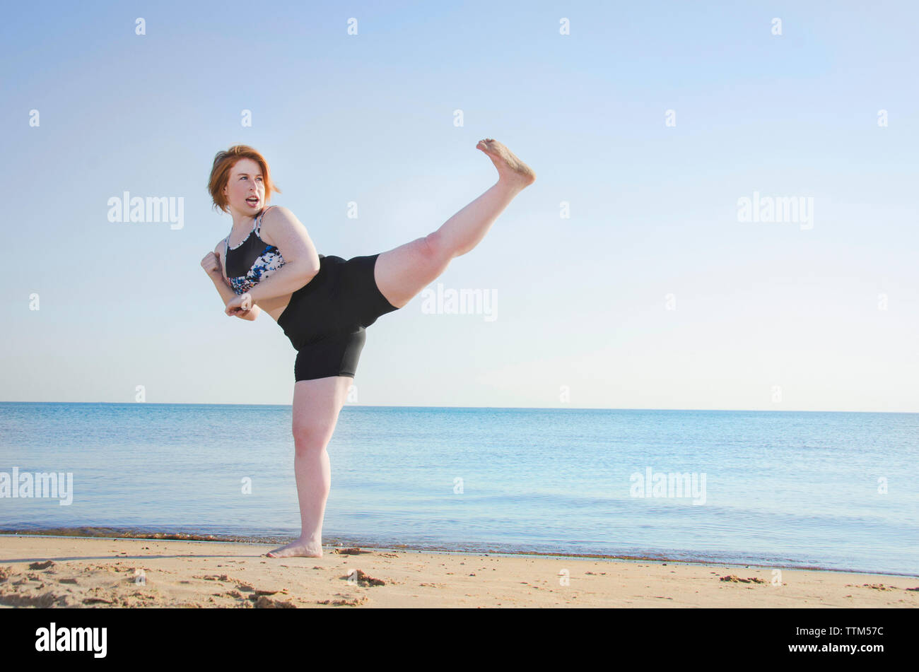 Donna praticano kickboxing a beach contro il cielo chiaro Foto Stock