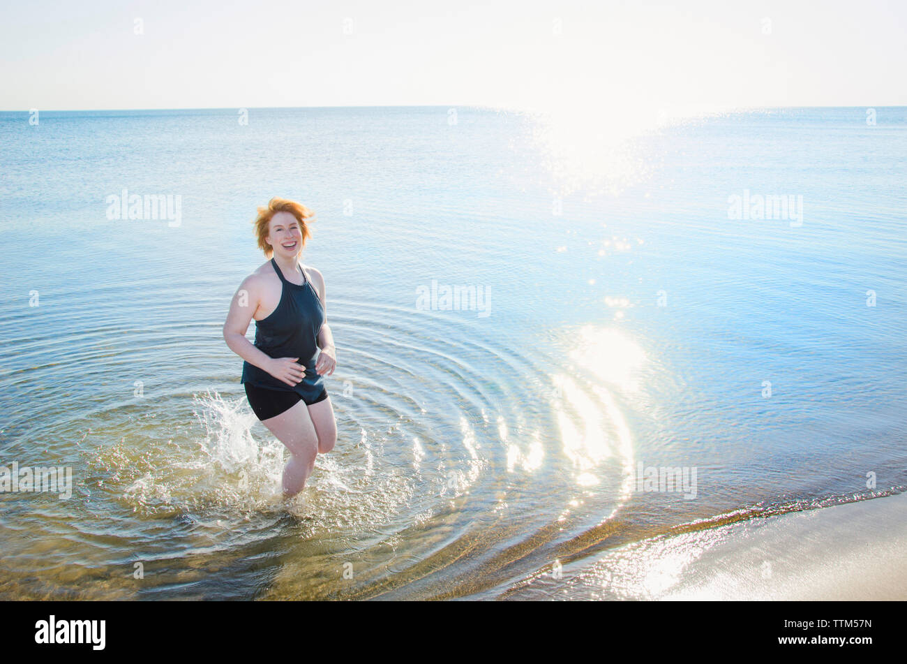 Elevato angolo di visione della donna felice in mare sulla riva contro il cielo chiaro Foto Stock Elevato angolo di visione della donna felice in mare sulla riva contro il cielo chiaro Foto Stock