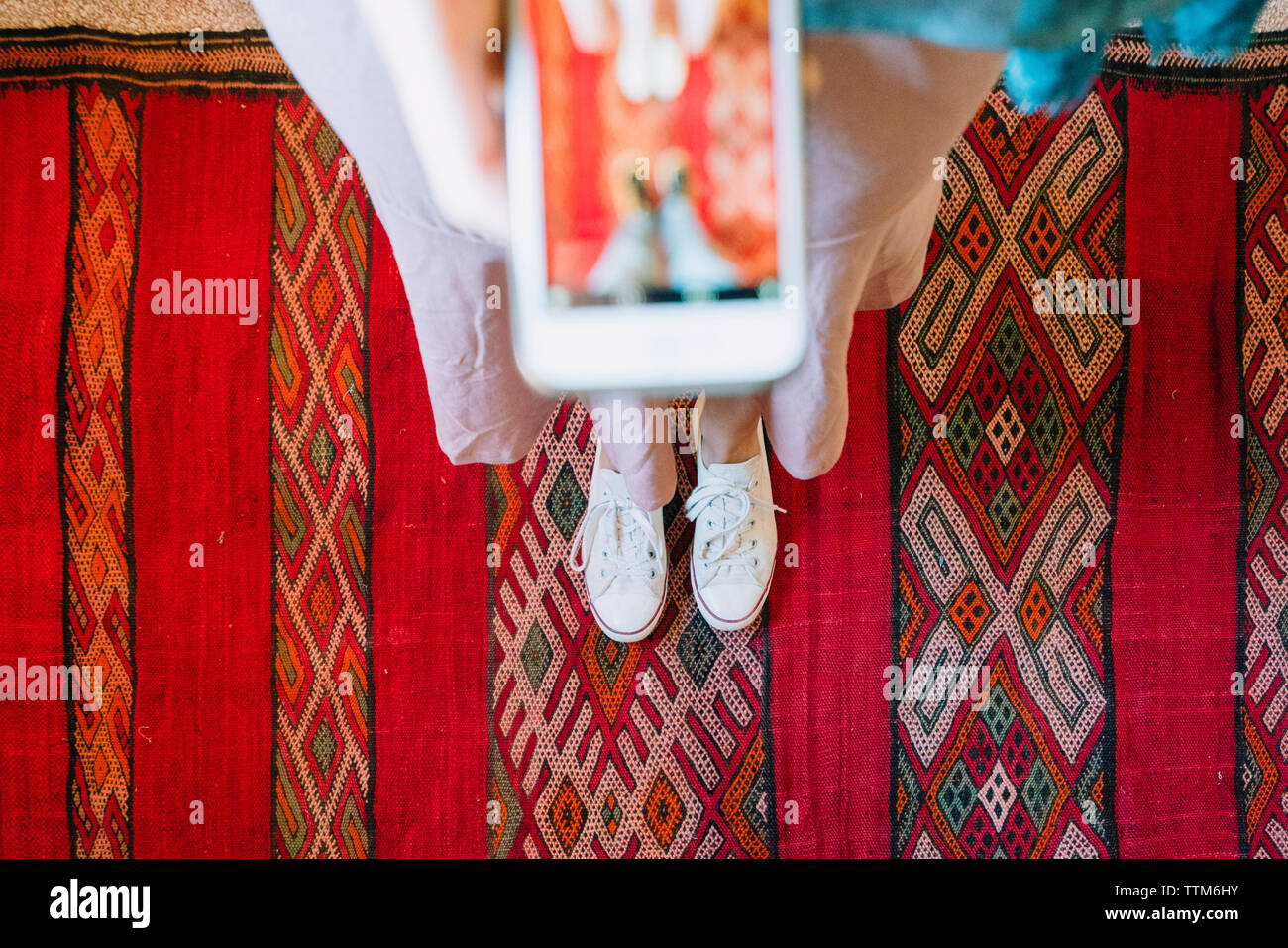 Sezione bassa di donna fotografare con smart phone mentre si sta in piedi sul tappeto tradizionale Foto Stock