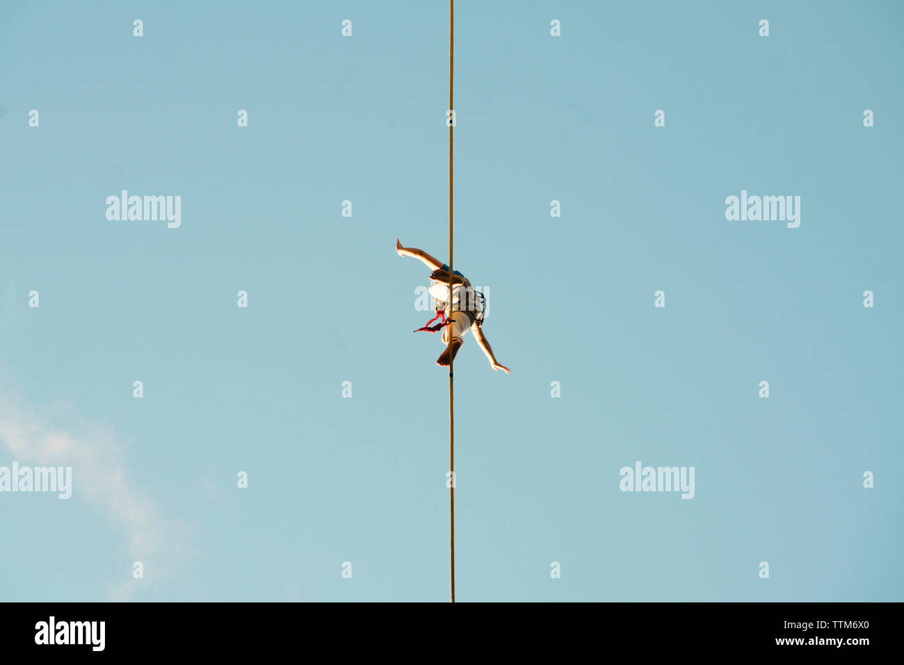 Basso angolo di visione dell'uomo slacklining contro il cielo blu e chiaro durante la giornata di sole Foto Stock