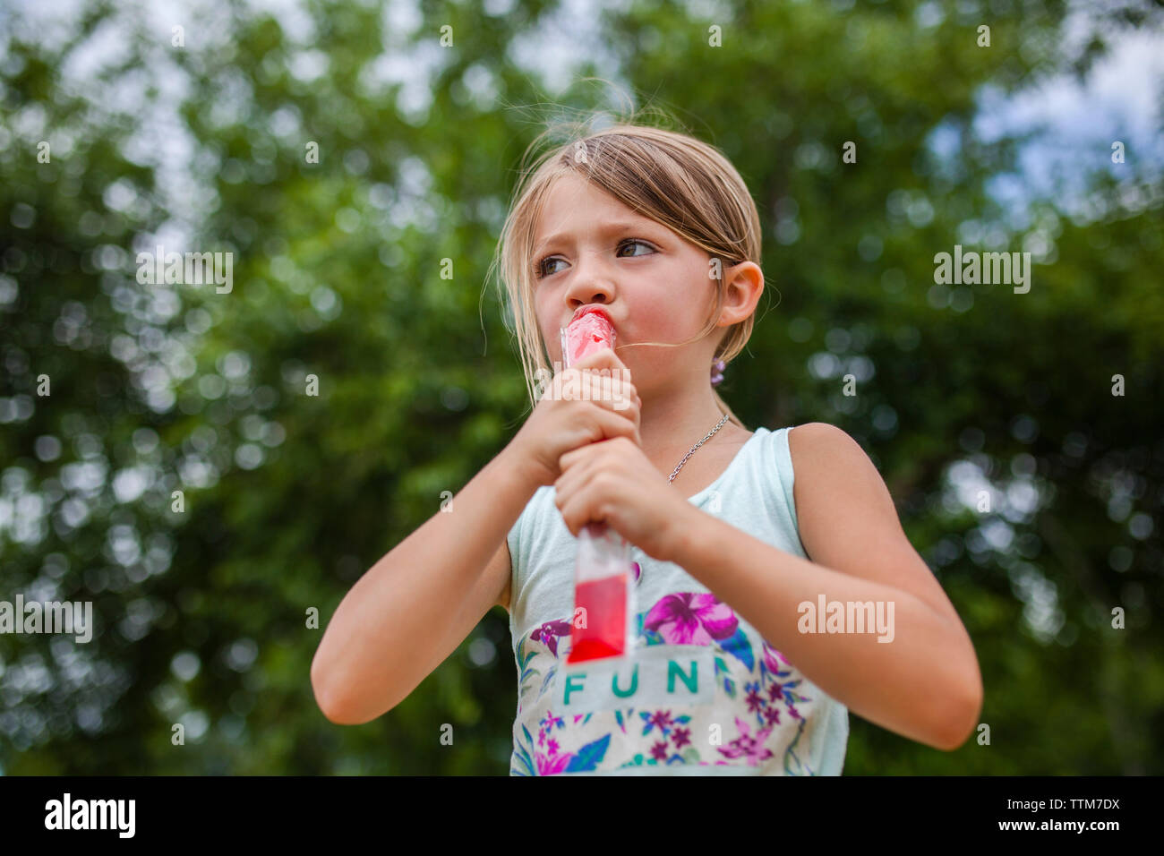 Basso angolo vista della ragazza che guarda lontano mentre mangia ghiaccio aromatizzato al park Foto Stock