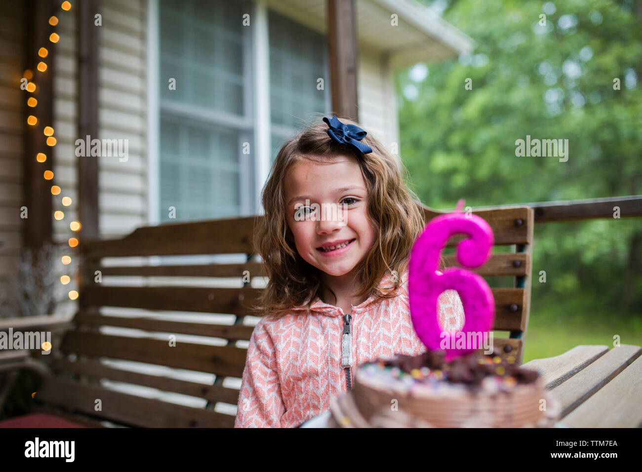 Ritratto di felice ragazza seduta da torta di compleanno con il numero 6 la candela al portico Foto Stock