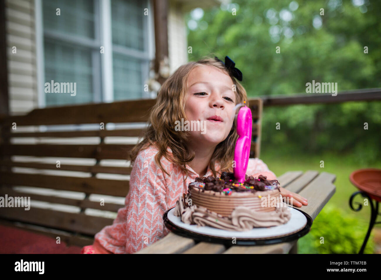 Ragazza soffiando fuori numero 6 candela sulla torta di compleanno al portico Foto Stock