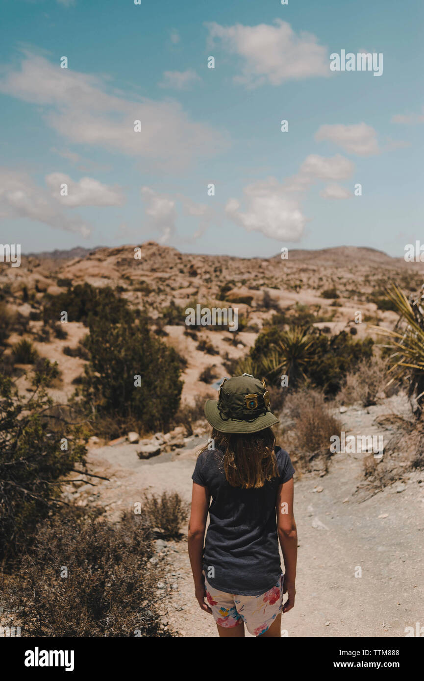 Vista posteriore di una ragazza che indossa hat in piedi sul deserto contro sky durante la giornata di sole Foto Stock