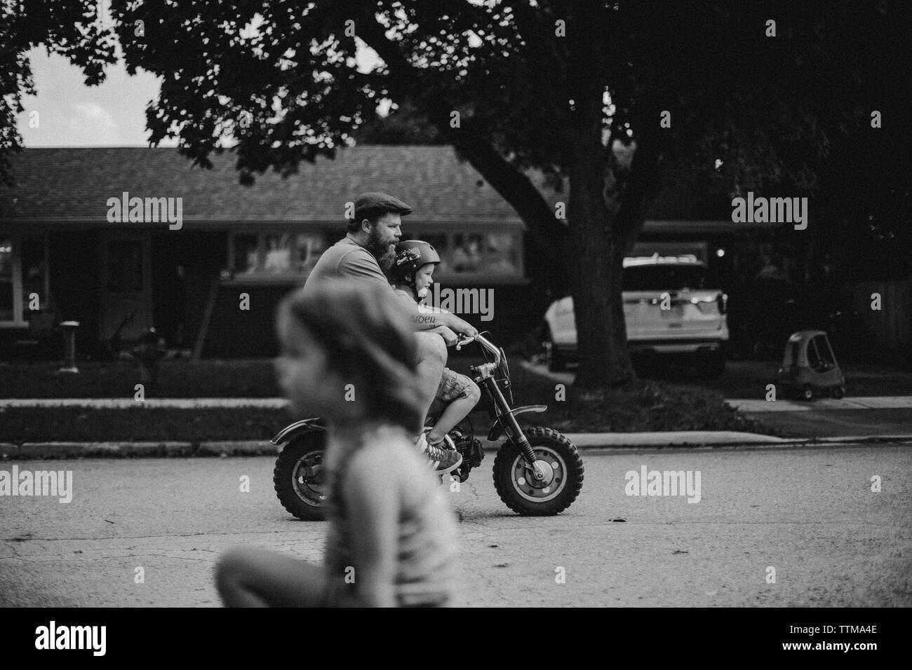 Un ragazzo corse il suo moto con suo padre mentre la sorella si affaccia su Foto Stock