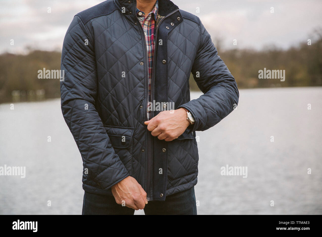 Sezione mediana dell'uomo zippare giacca di pelle mentre in piedi dal lago contro sky in foresta Foto Stock