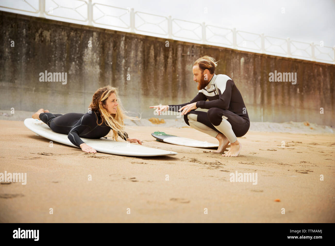 Uomo che parla di donna sdraiata sulla tavola da surf in spiaggia Foto Stock