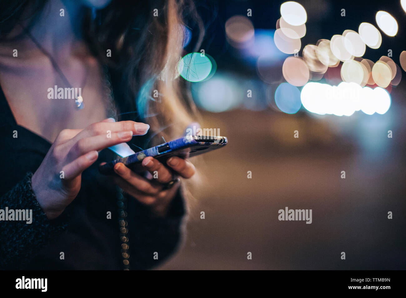 Sezione mediana della donna utilizzando smart phone permanente, mentre all'esterno di notte Foto Stock