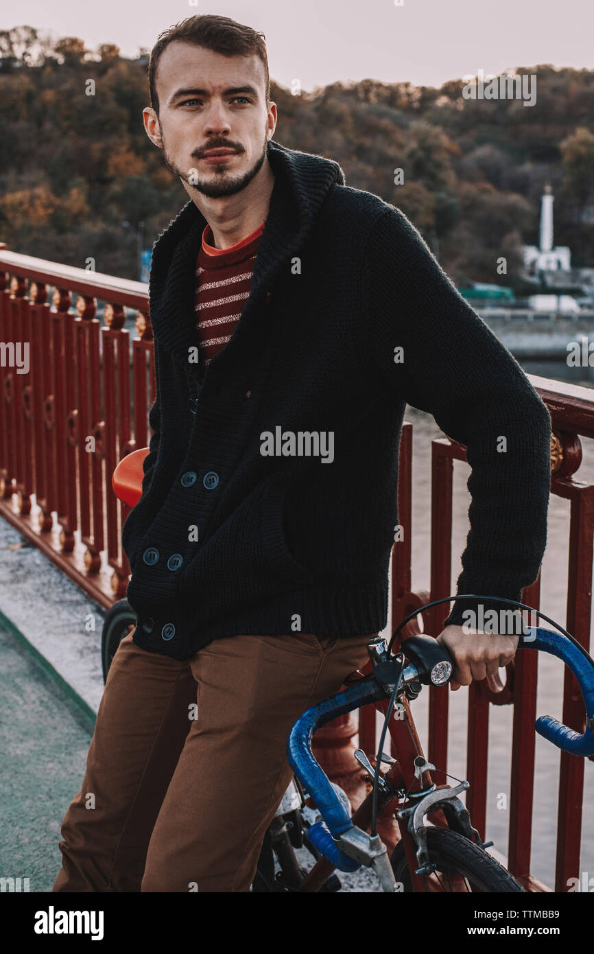 Considerato l uomo che guarda lontano mentre in piedi con la bicicletta sul ponte contro gli alberi durante il tramonto Foto Stock