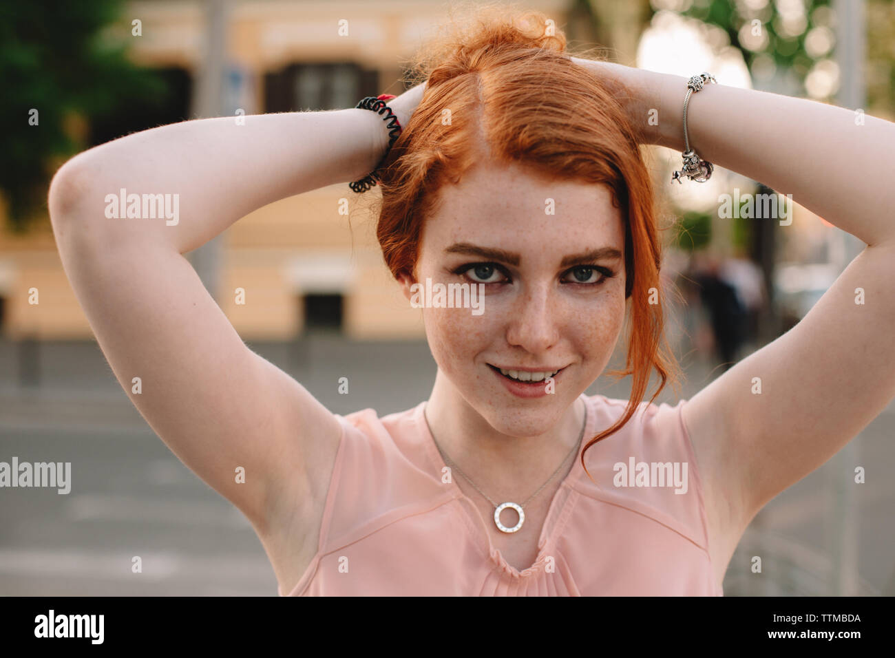 Ritratto di giovane donna redheaded holding capelli mentre in piedi in città Foto Stock