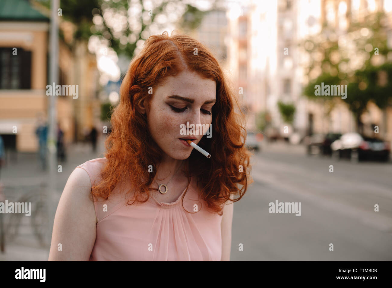 Redheaded giovane donna con la sigaretta in piedi sulle strade della città Foto Stock