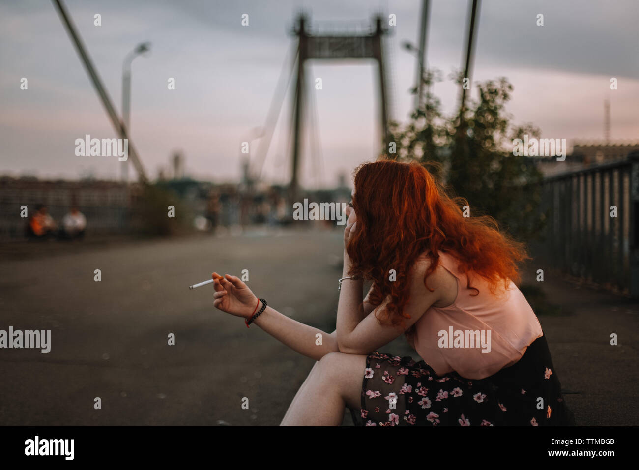 Giovane donna redheaded Sigaretta fumare mentre è seduto sul ponte Foto Stock