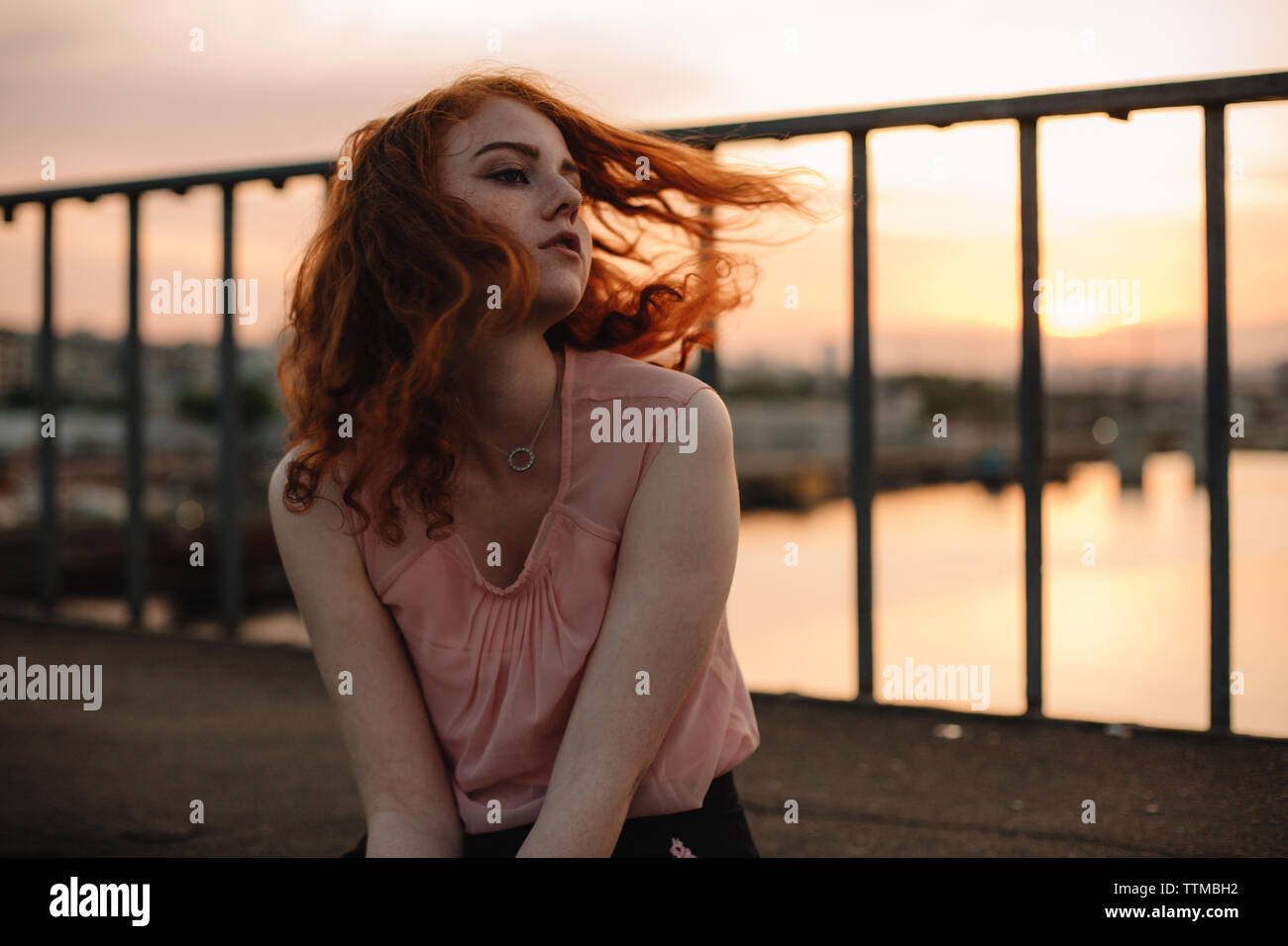 Testa rossa ragazza adolescente tossing capelli mentre è seduto sul ponte al tramonto Foto Stock