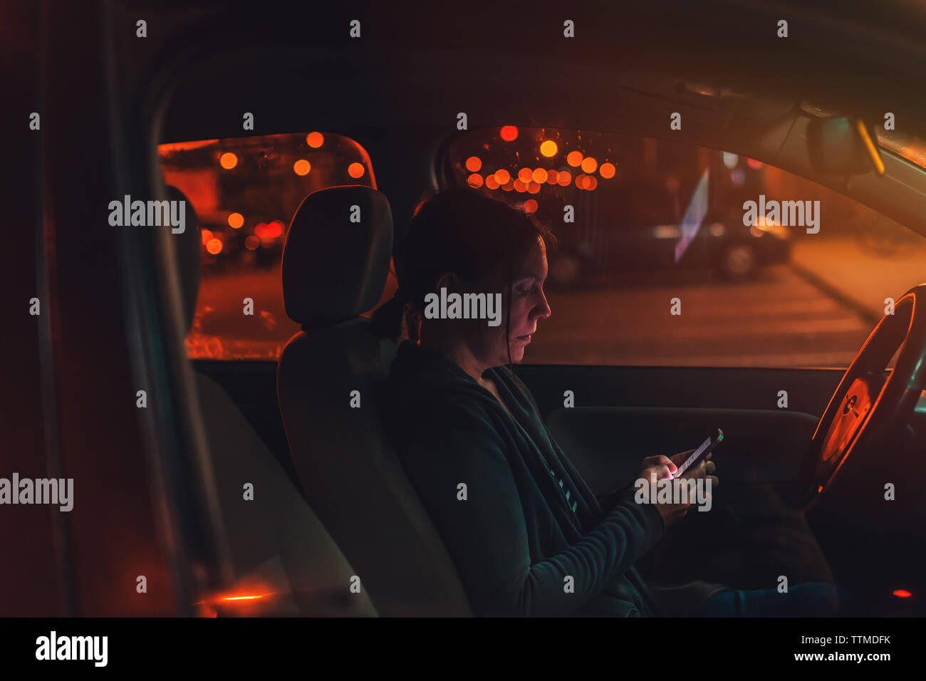 Utilizzo di smart phone in macchina di notte, il fuoco selettivo bassa immagine chiave della persona di sesso femminile con il cellulare in mano Foto Stock
