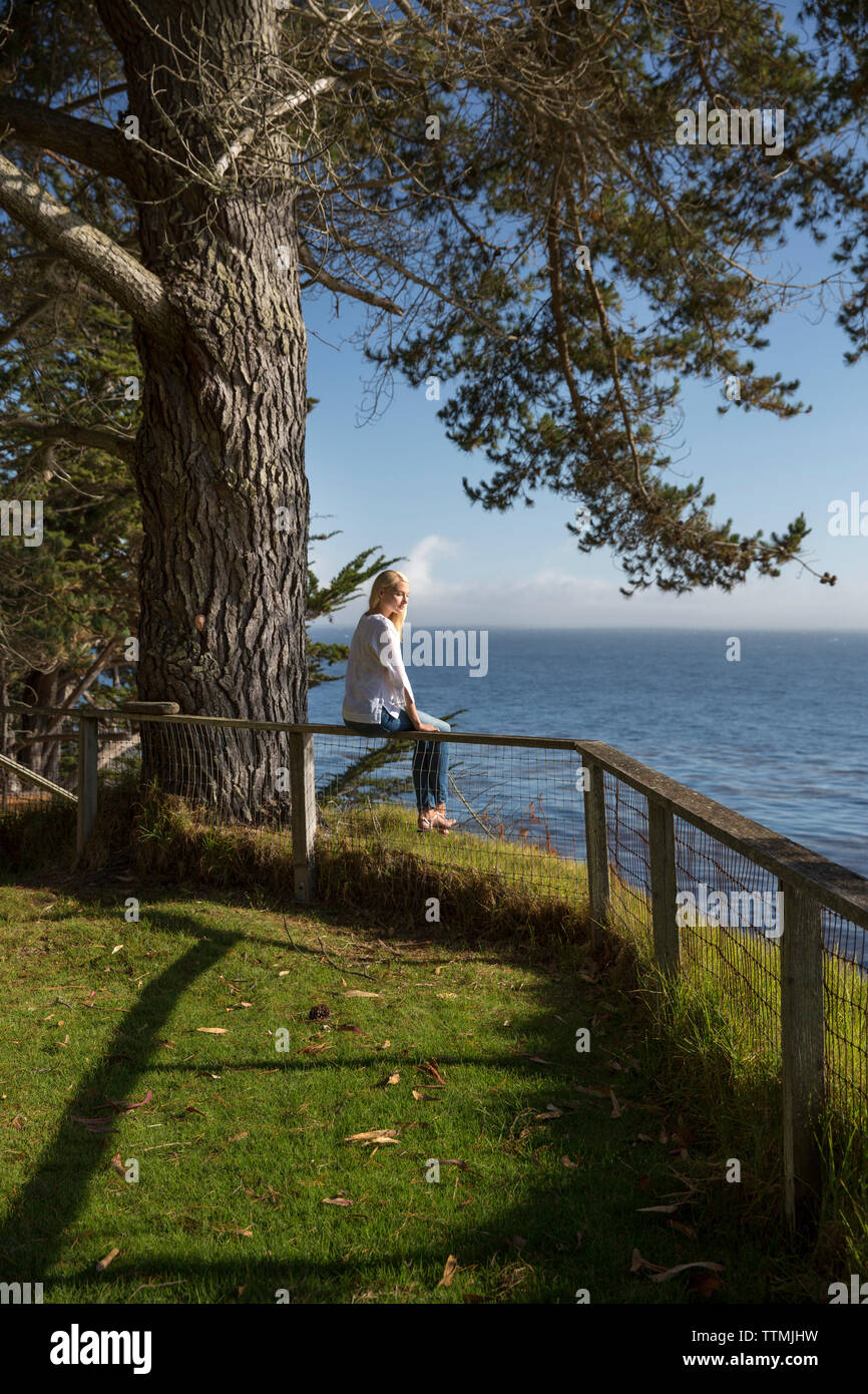 Stati Uniti, California, Big Sur, Esalen, donna siede sul recinto vicino alla Fattoria e gode del sole e la vista dell'Oceano Pacifico, il Esalen Institute Foto Stock