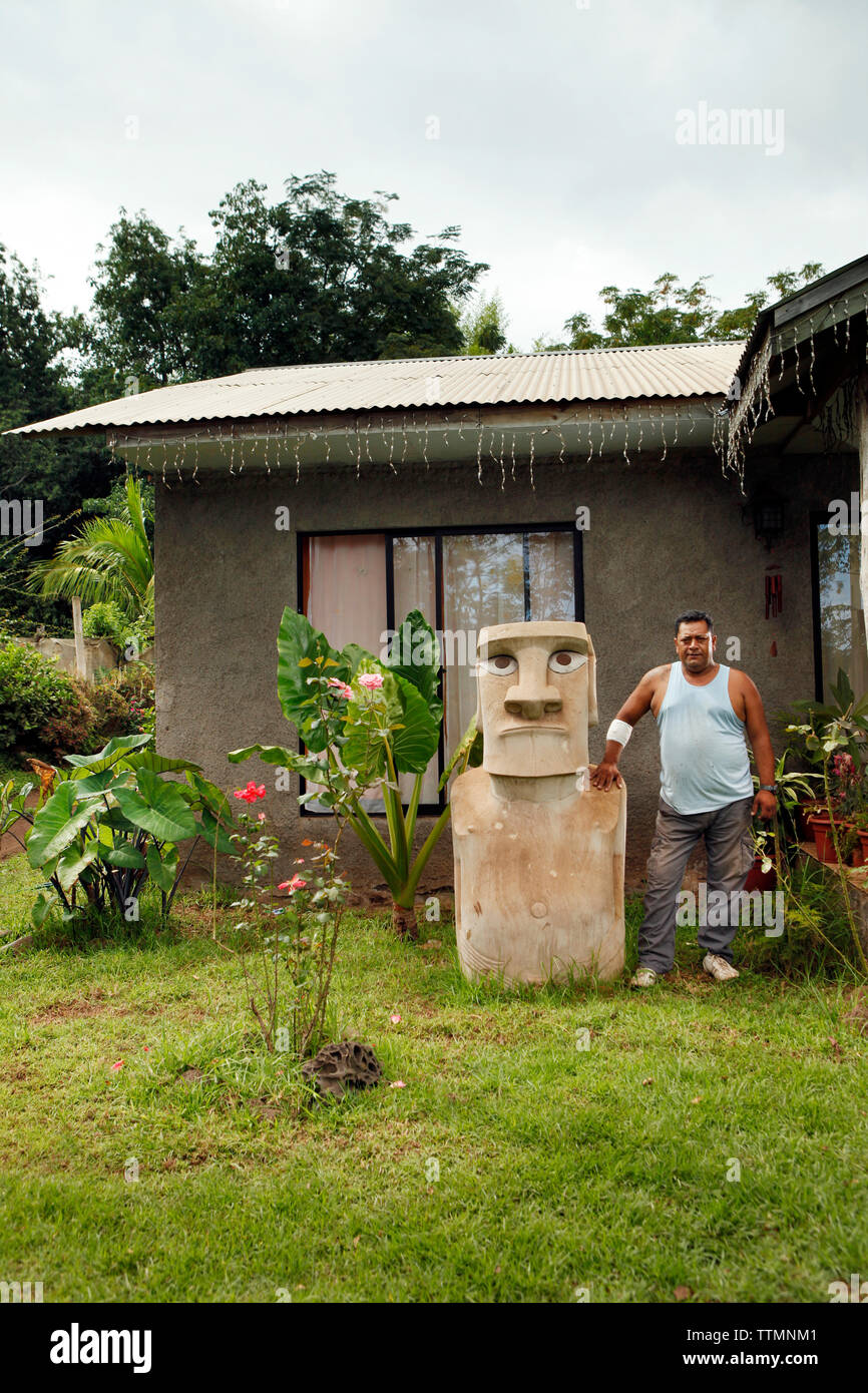 ISOLA di pasqua, CILE, Isla de Pascua, Rapa Nui, un uomo del posto si trova fuori dalla sua casa accanto a una statua Moai a Hanga Roa Foto Stock