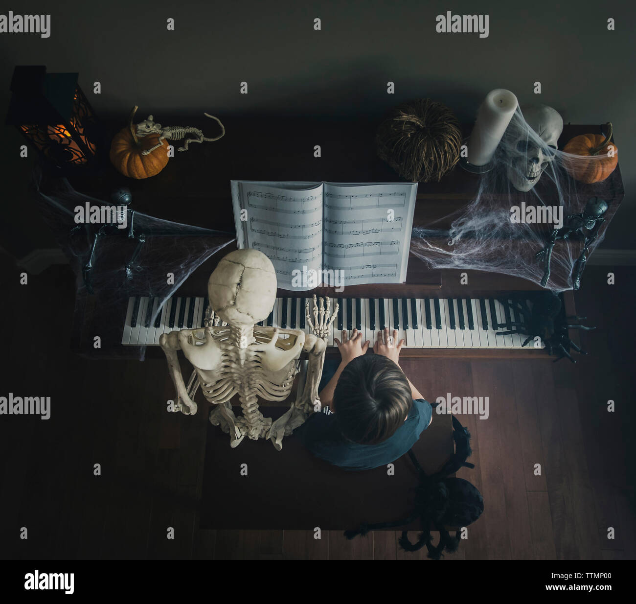 Angolo di Alta Vista del ragazzo suonare il pianoforte mentre è seduto dallo scheletro durante il periodo di Halloween Foto Stock