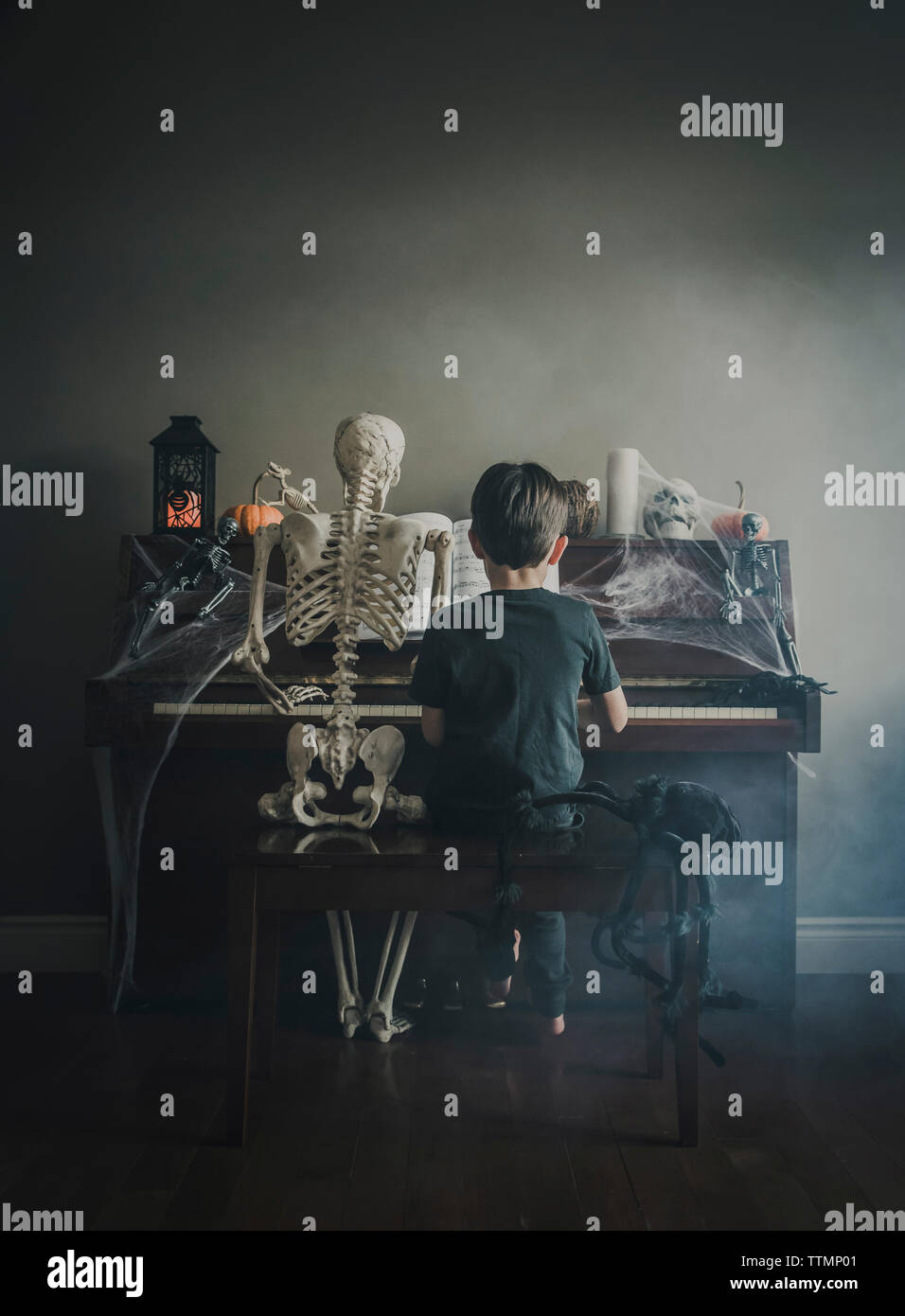 Vista posteriore del ragazzo suonare il pianoforte mentre è seduto dallo scheletro durante il periodo di Halloween Foto Stock