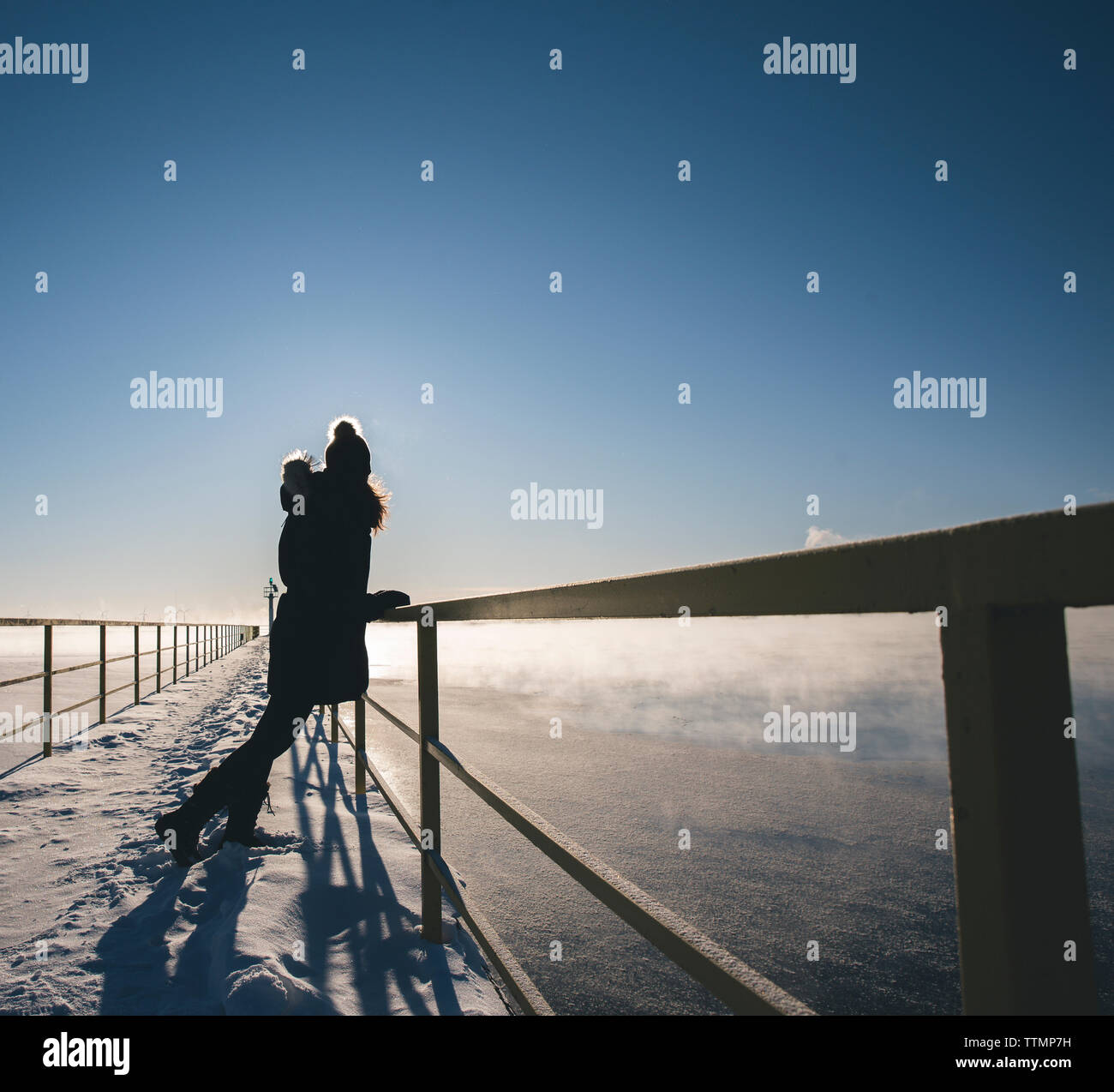 Per tutta la lunghezza della donna in piedi sulla coperta di neve pier dalla ringhiera oltre il lago ghiacciato contro sky Foto Stock