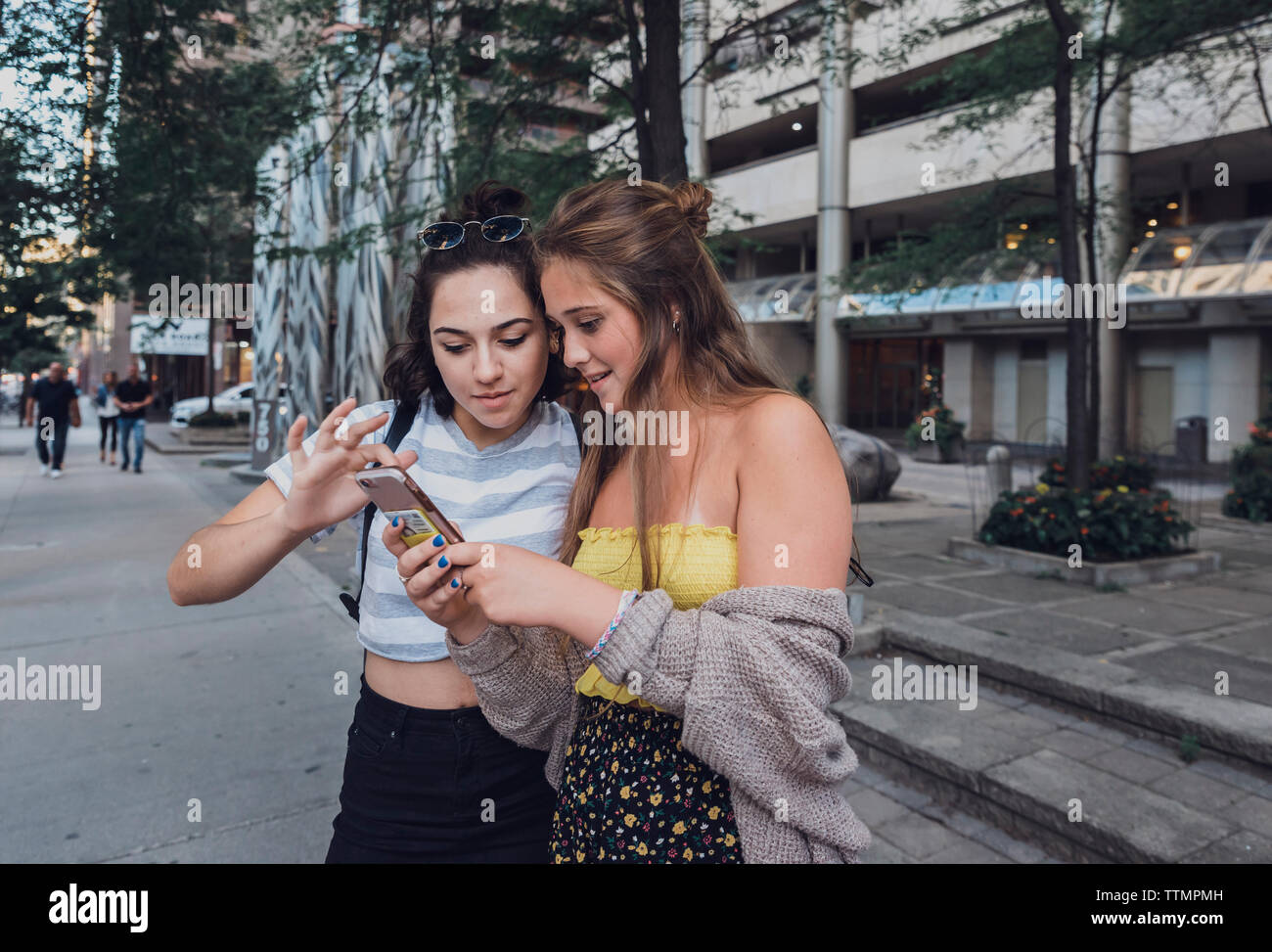 Gli amici utilizzando smart phone mentre si sta in piedi sul marciapiede in città Foto Stock