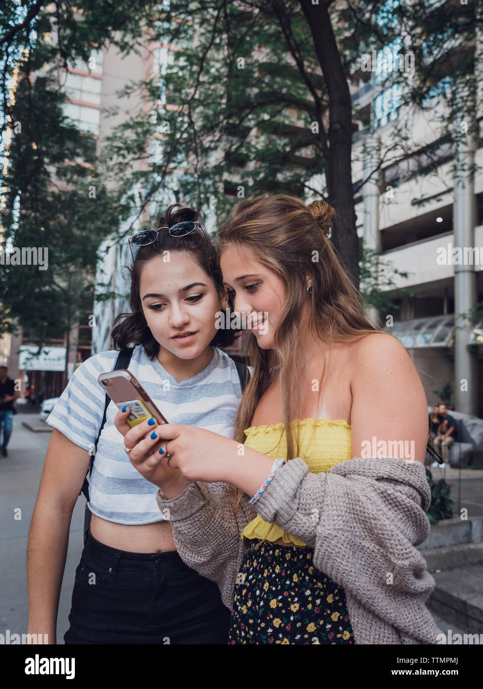 Gli amici utilizzando il telefono cellulare mentre si sta in piedi sul marciapiede in città Foto Stock
