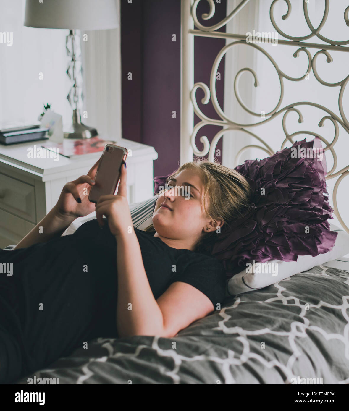 Ragazza adolescente utilizzando smart phone mentre giaceva sul letto di casa Foto Stock