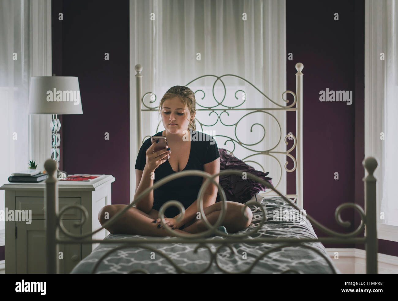 Ragazza adolescente utilizzando smart phone mentre è seduto sul letto di casa Foto Stock