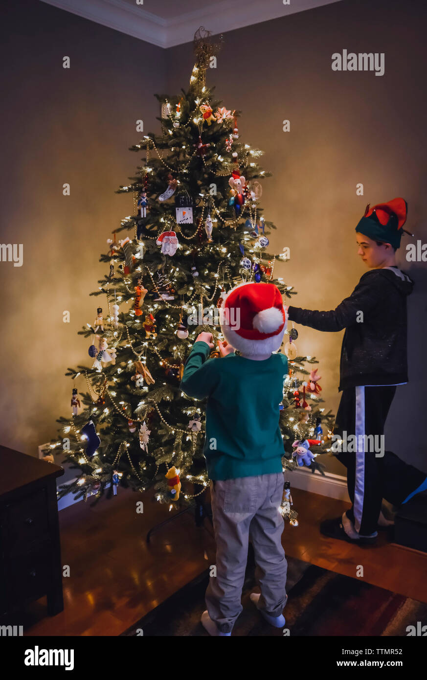 Due ragazzi decorare albero di Natale indossando cappelli di festa. Foto Stock
