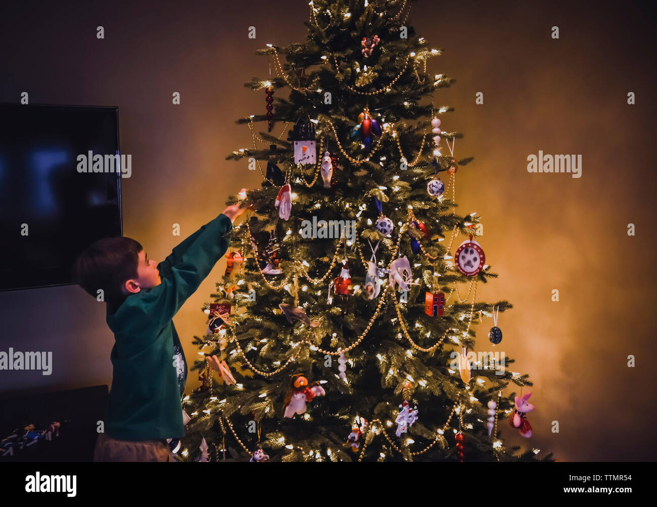 Ragazzo di raggiungere per mettere ornamenti su un albero di Natale. Foto Stock