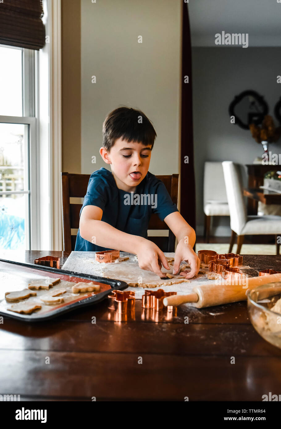 Ragazzo giovane rendendo i cookie con cookie cutters al tavolo. Foto Stock
