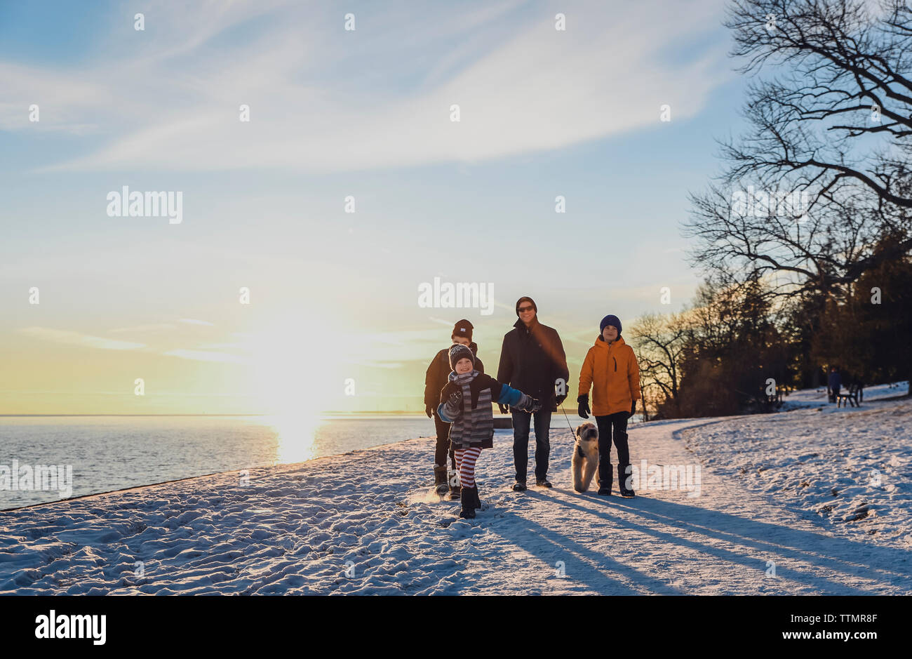 Padre e figli a piedi un cane lungo un sentiero innevato al tramonto. Foto Stock