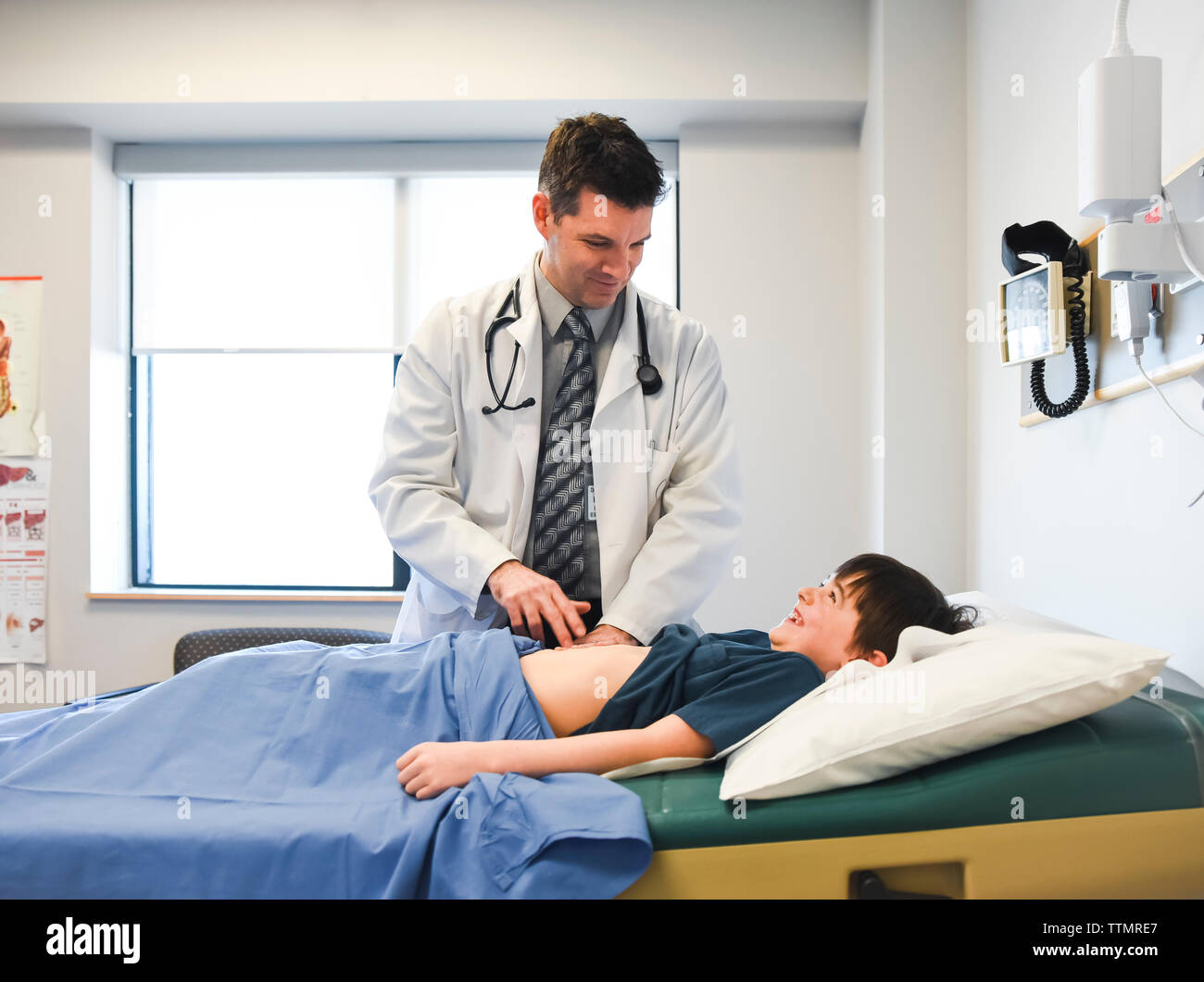 Medico esaminando l'addome del bambino su un tavolo di esame di una clinica. Foto Stock