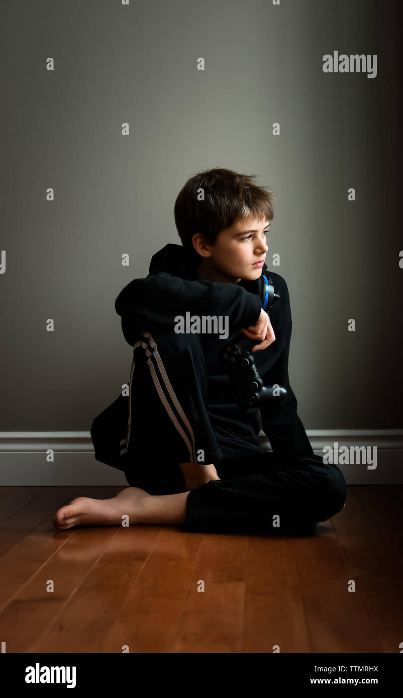 Preteen ragazzo seduto sul pavimento con i video game controller in mano. Foto Stock