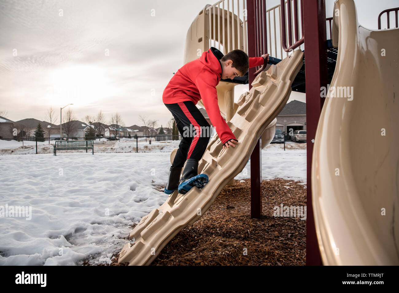 Ragazzo salendo sulla struttura di gioco in un parco innevato sul giorno d'inverno. Foto Stock