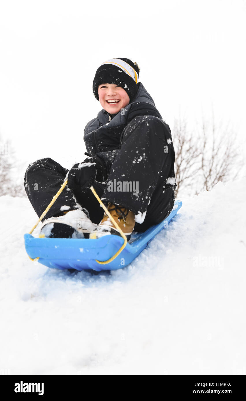 Sorridente ragazzo seduto su di una pista da slittino sulla neve collina su un giorno d'inverno. Foto Stock
