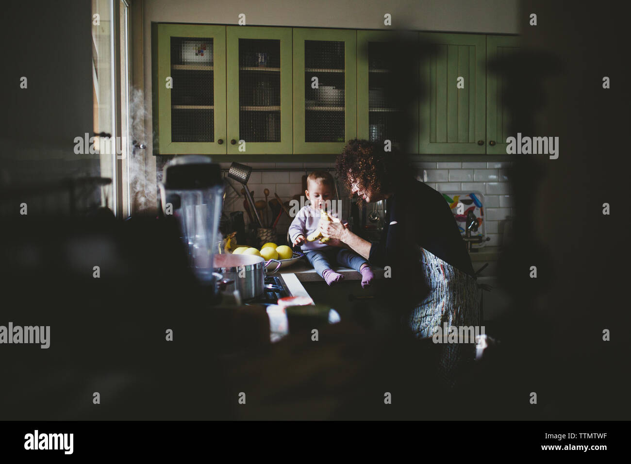 Giovane ragazza del bambino seduto sul gramma il bancone cucina mangiare banana Foto Stock