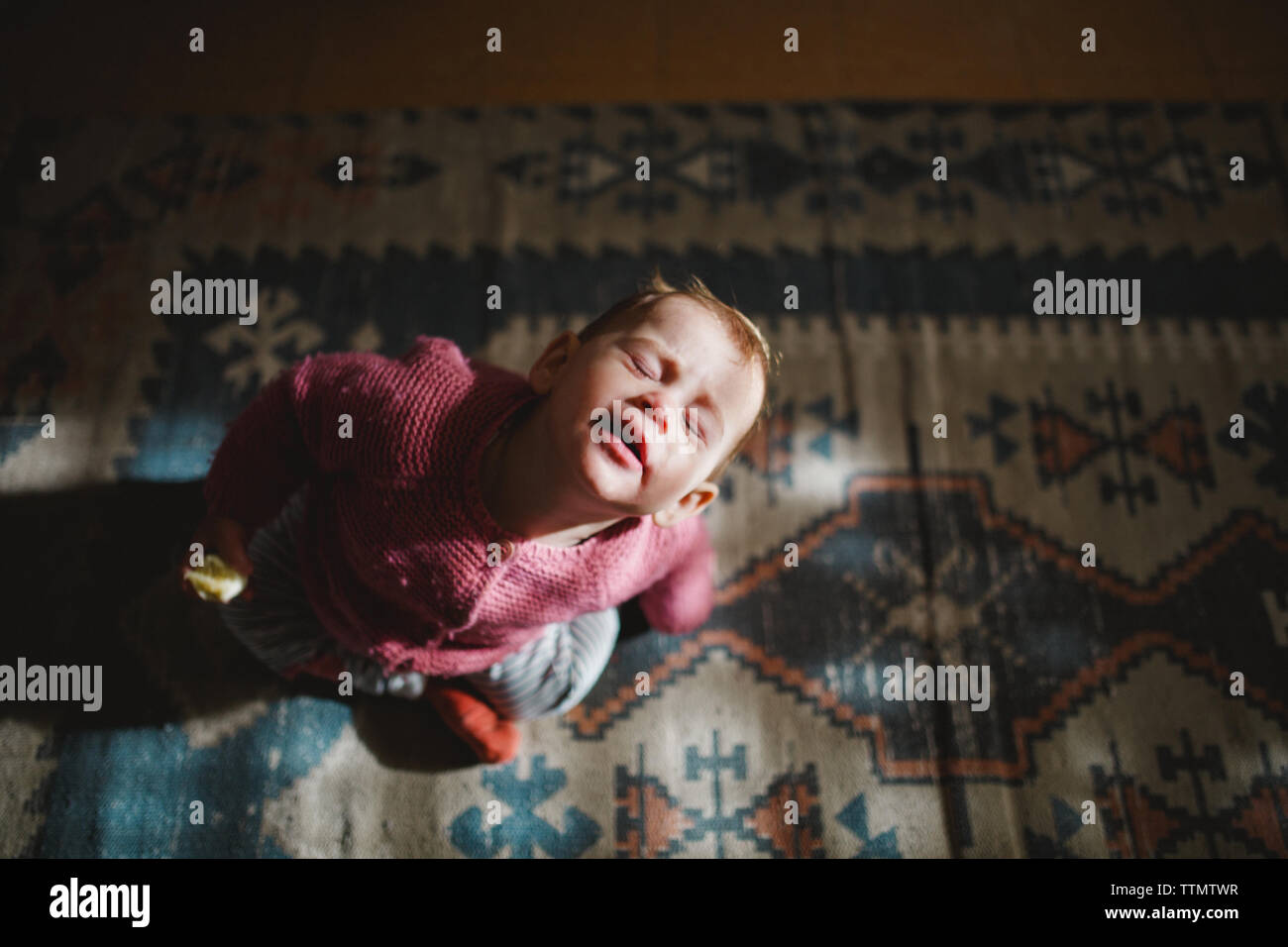 Un bambino ragazza seduta su un tappeto guardando verso l'alto con gli occhi chiusi Foto Stock